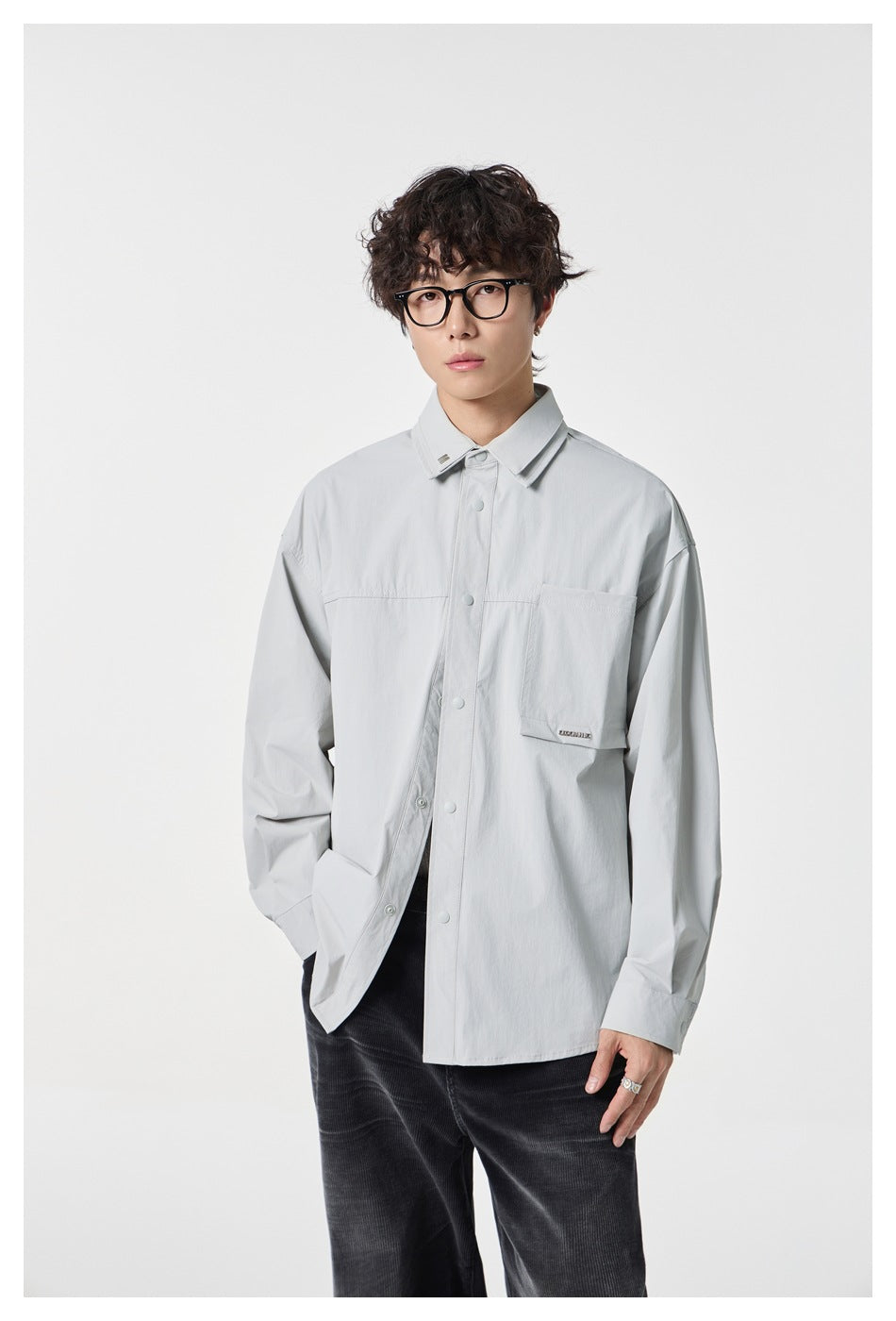 Man wearing a light gray oversized button-front shirt with chest pocket over dark corduroy pants