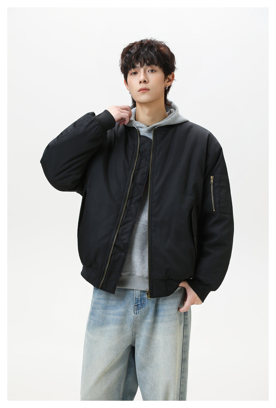 Model wearing black zip-front padded bomber jacket over a gray hoodie and light-wash jeans