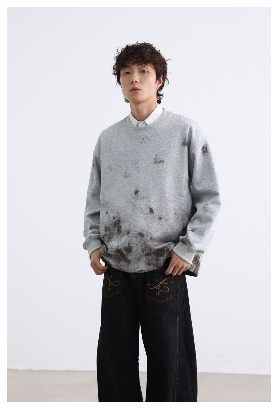 Model wearing a light gray distressed sweatshirt with ribbed cuffs and collar, paired with wide black jeans.