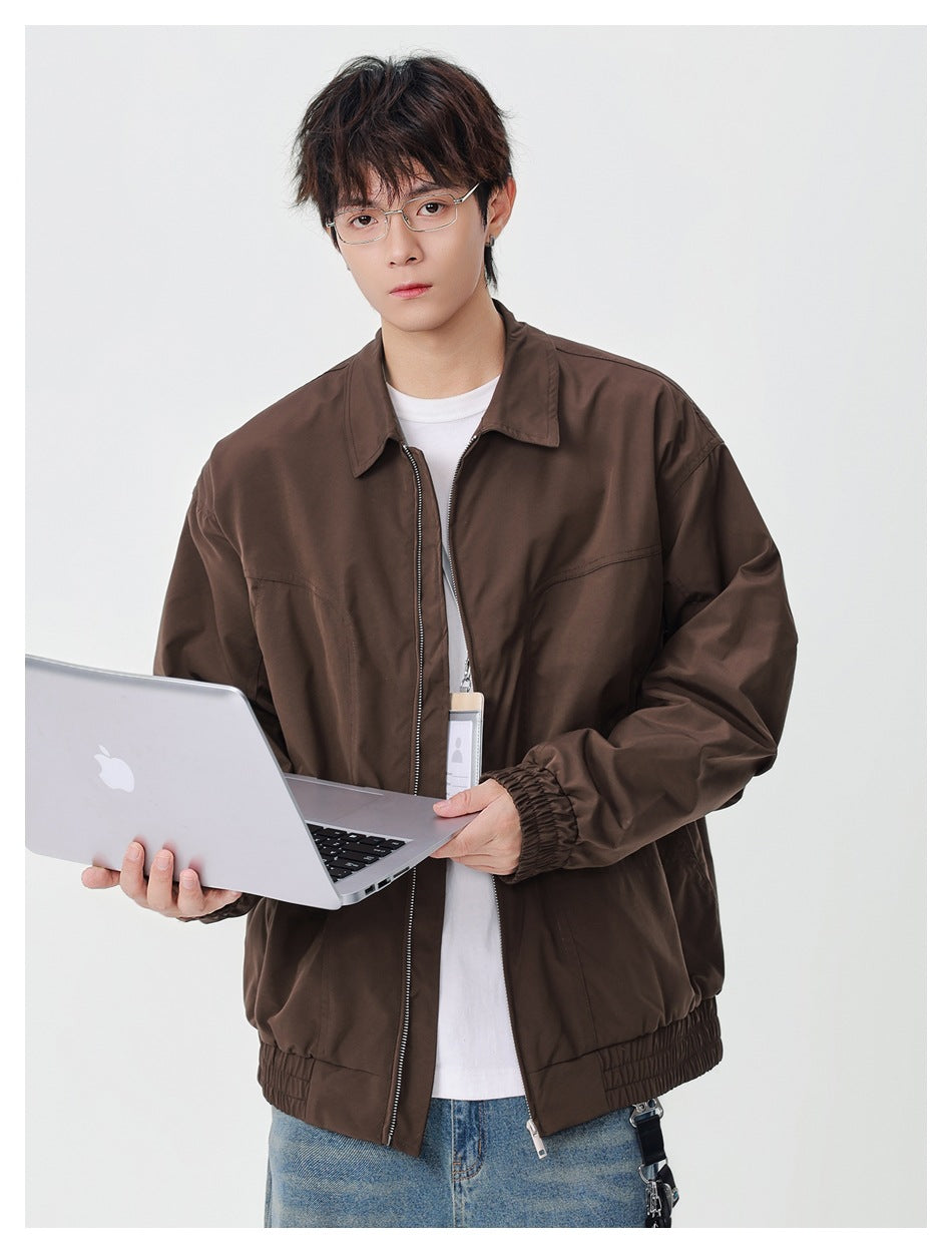 Model wearing a brown collared zip jacket with elastic cuffs and hem, holding an open silver laptop.