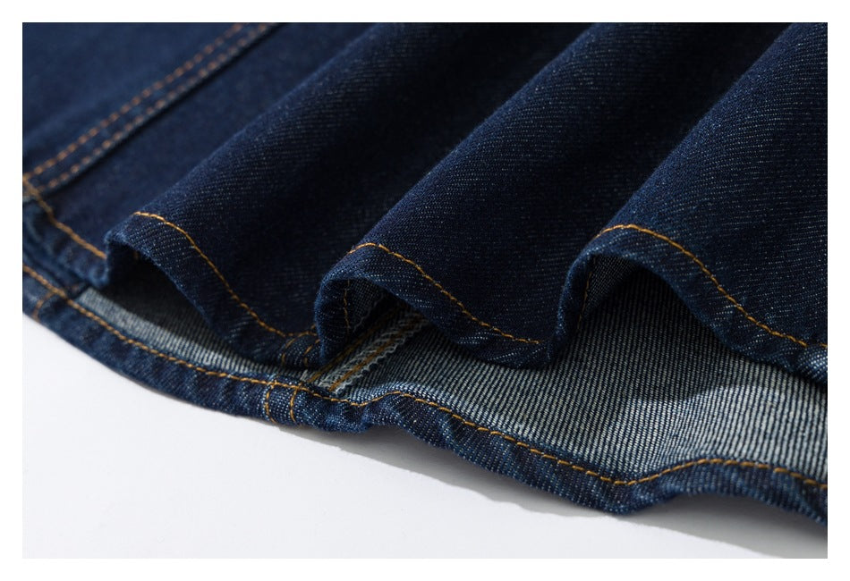 Close-up of a dark indigo denim hem with golden-orange stitching and the reverse weave visible.