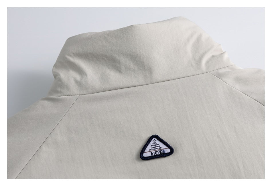 Close-up of a beige jacket’s back collar and shoulder seams, with a small triangular embroidered patch.