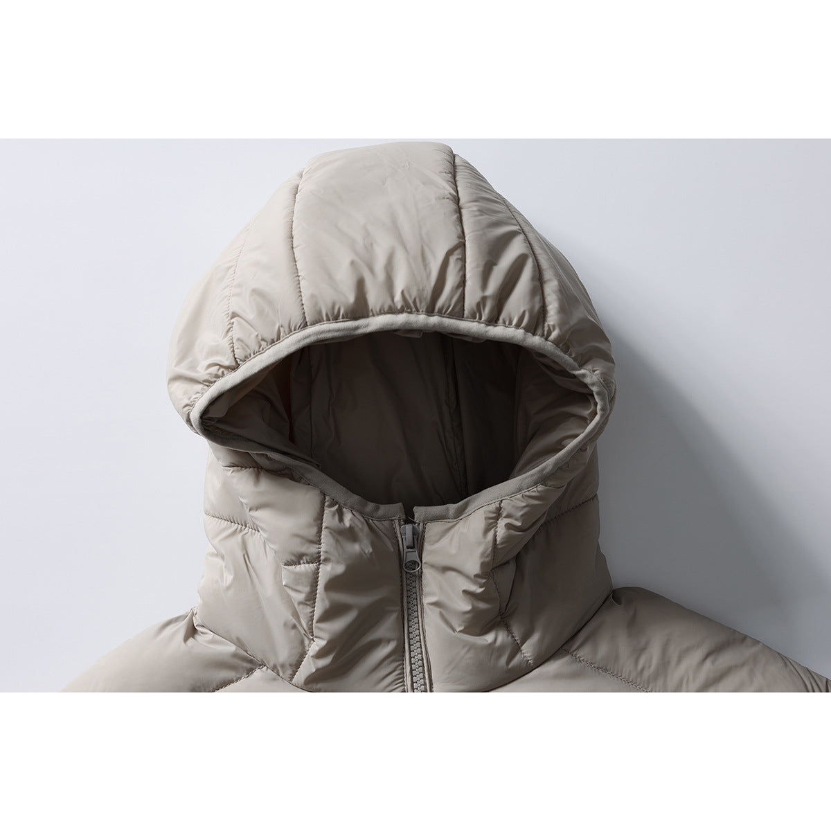 Close-up of a light taupe padded jacket's oversized hood, dark lining, and front zipper.