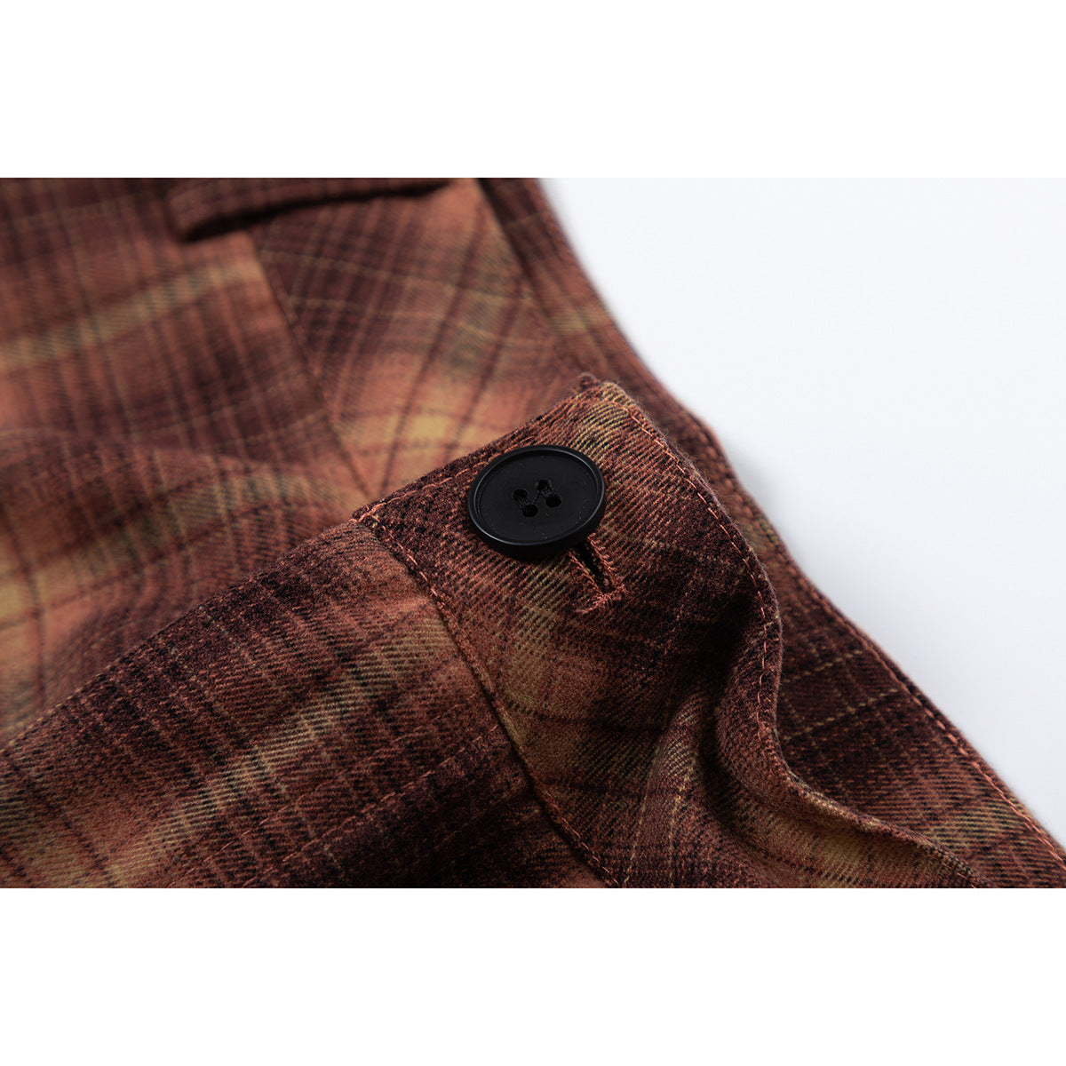 Close-up of a black button and waistband on brown-and-tan plaid trousers.