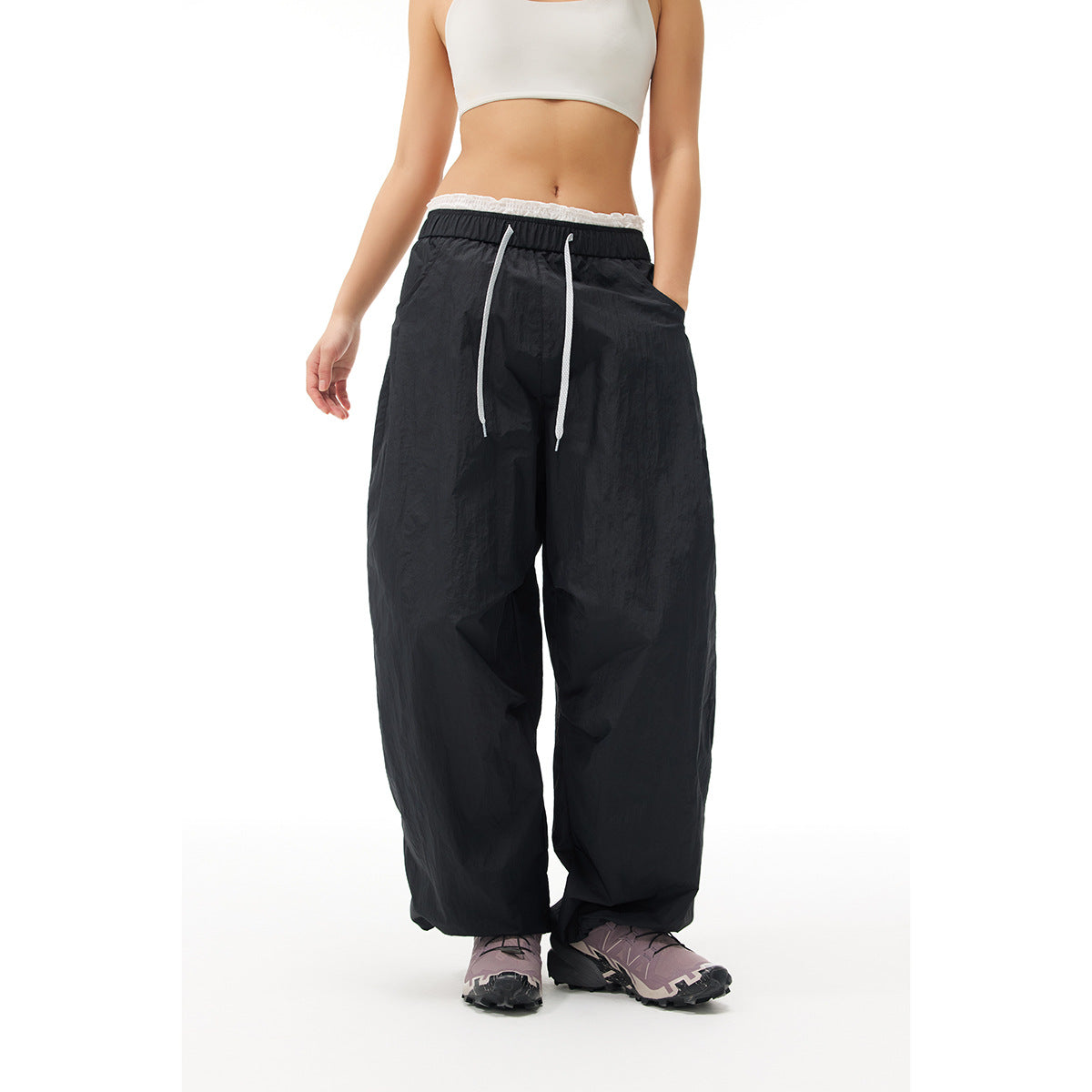 Front view of a model wearing loose black pants with a white drawstring and elastic waist.