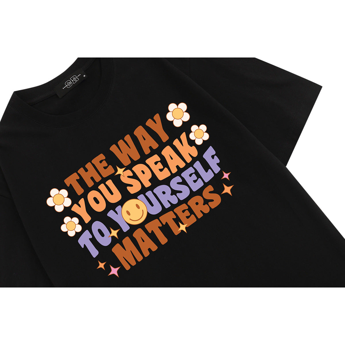 Close-up of a black T-shirt with a colorful floral slogan graphic reading “The way you speak to yourself matters.”