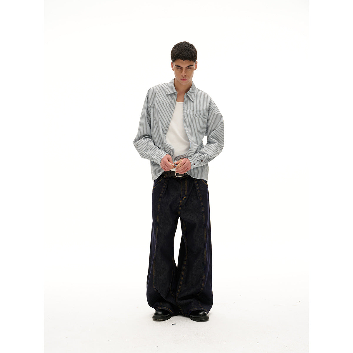 Model wearing a gray pinstriped zip-front shirt over a white tee with very wide dark jeans.