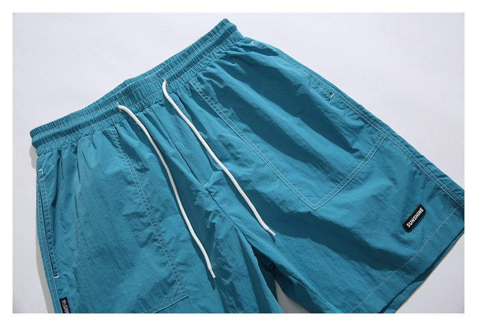 Close-up of bright blue shorts showing the elastic waistband, white drawstrings, front pockets, and SUNSHINE patch.
