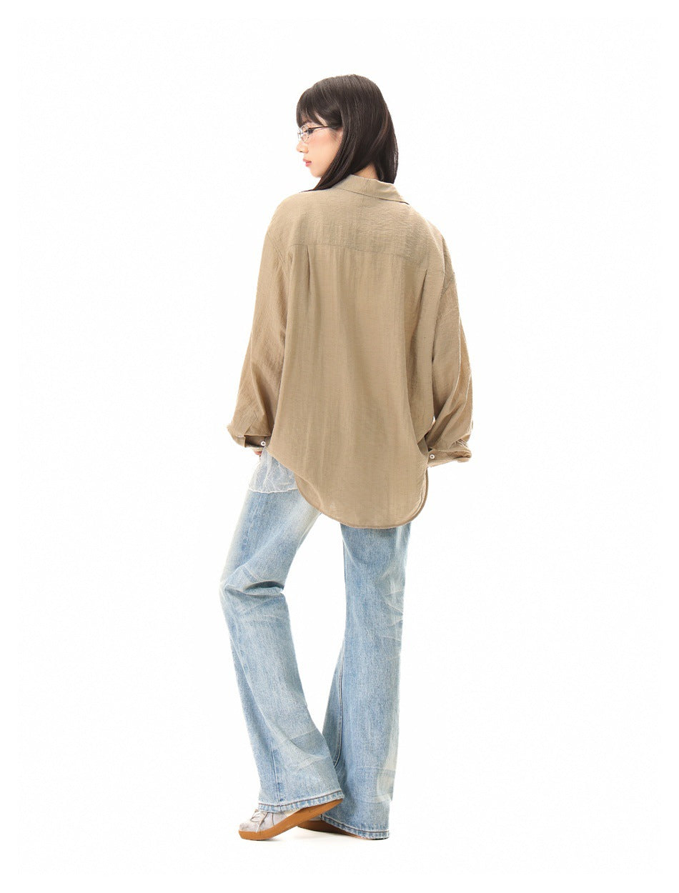 Rear three-quarter view of a model wearing a tan oversized shirt with a curved hem and light blue jeans.