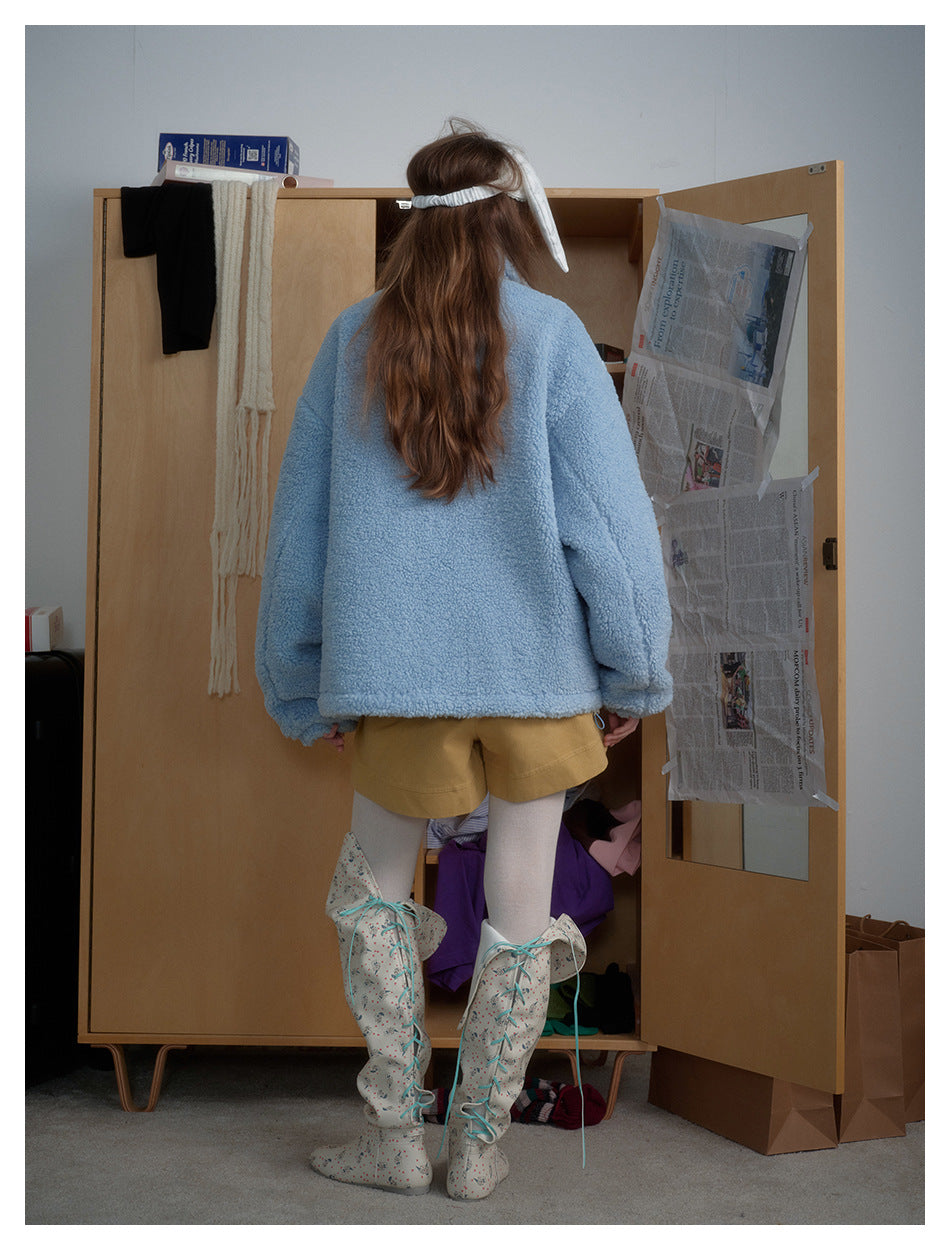 Back view of a model wearing an oversized, plain light-blue plush jacket with mustard shorts.