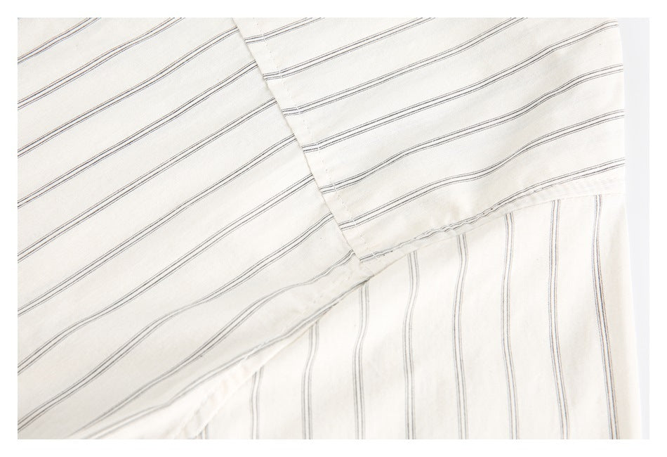 Close-up of overlapping off-white shirt fabric with fine dark stripes and stitched edges.