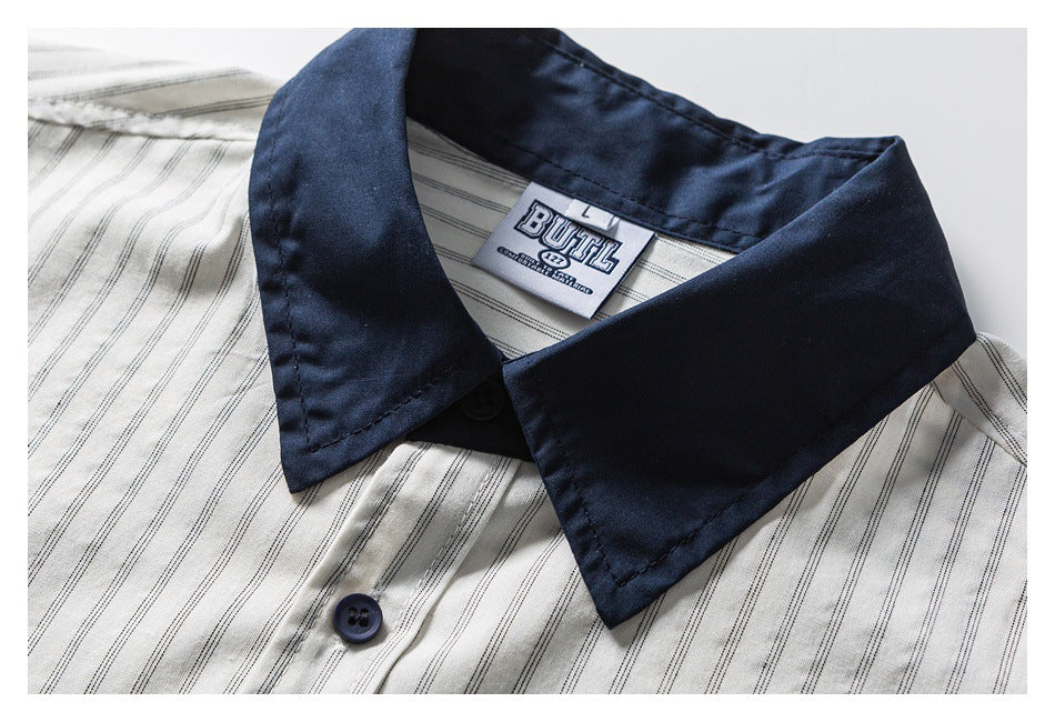 Close-up of a cream striped shirt showing its navy pointed collar, button, and sewn neck label.