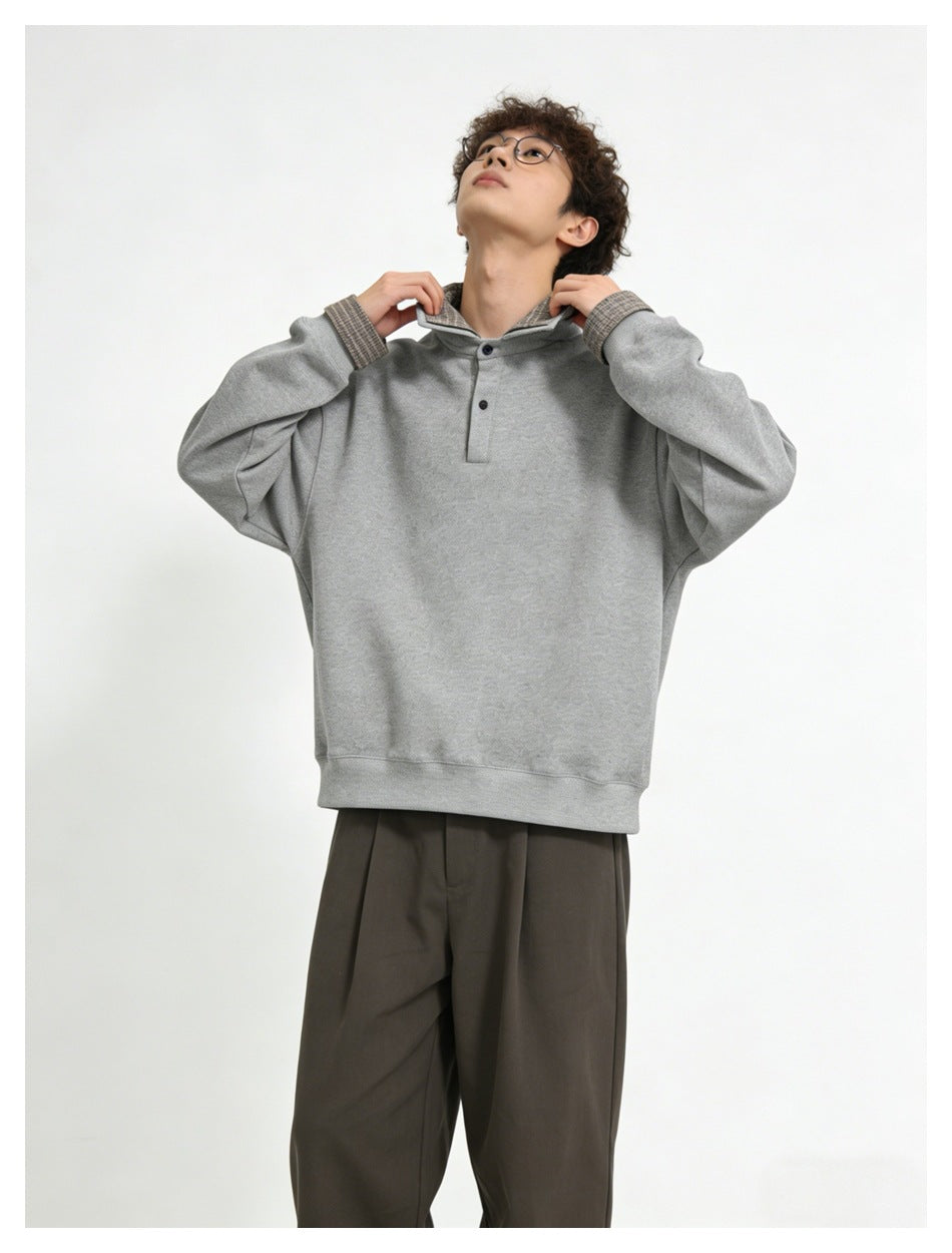 Model adjusting the collar of a light gray pullover with plaid lining and cuffs, paired with taupe trousers.