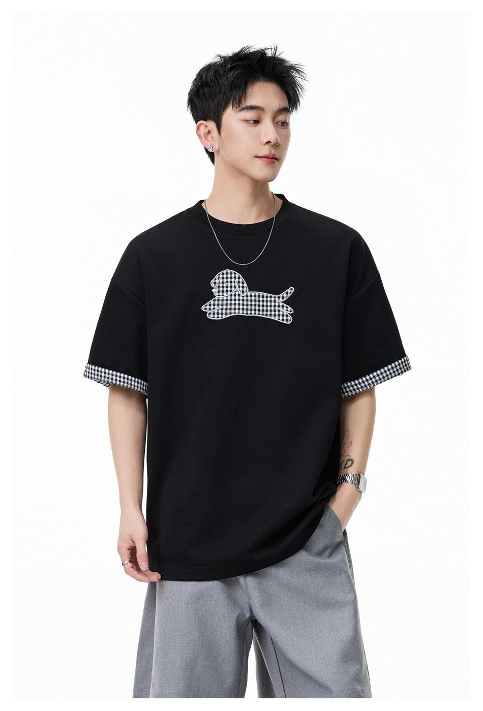 Model wearing black oversized T-shirt with gingham dog appliqué, gingham-lined turned-up sleeves and gray pants