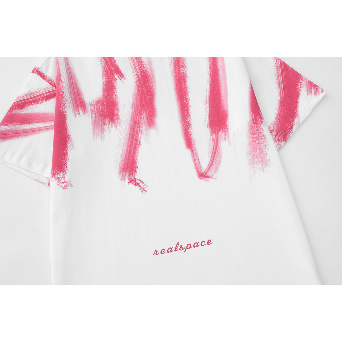 Close-up of pink brushstroke graphics and small script lettering on a white T-shirt.