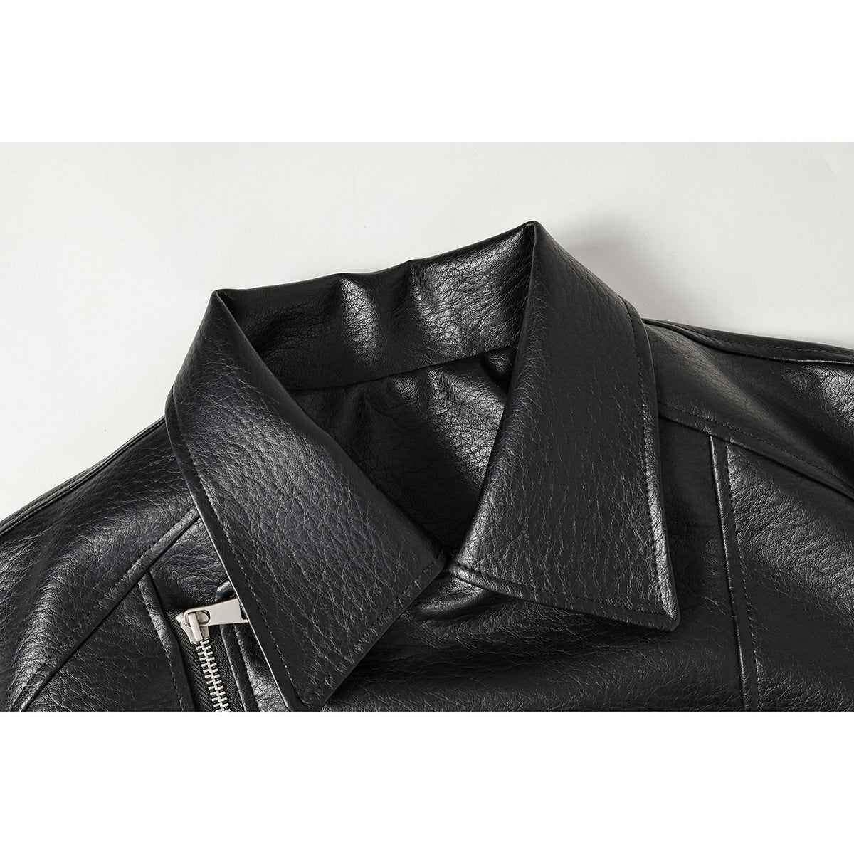 Close-up of a black jacket's wide pointed collar, stitched panels, and silver zipper on a white background.