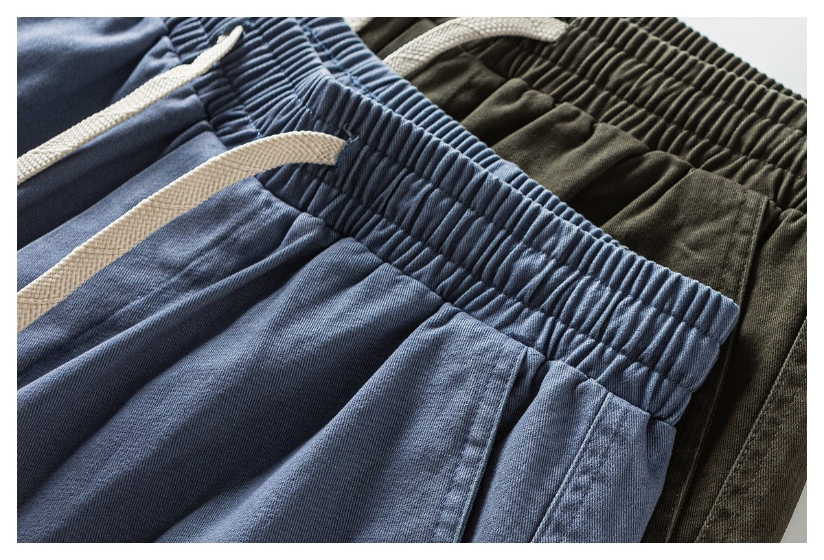 Close-up of blue and olive pants with gathered elastic waistbands and cream drawstrings.
