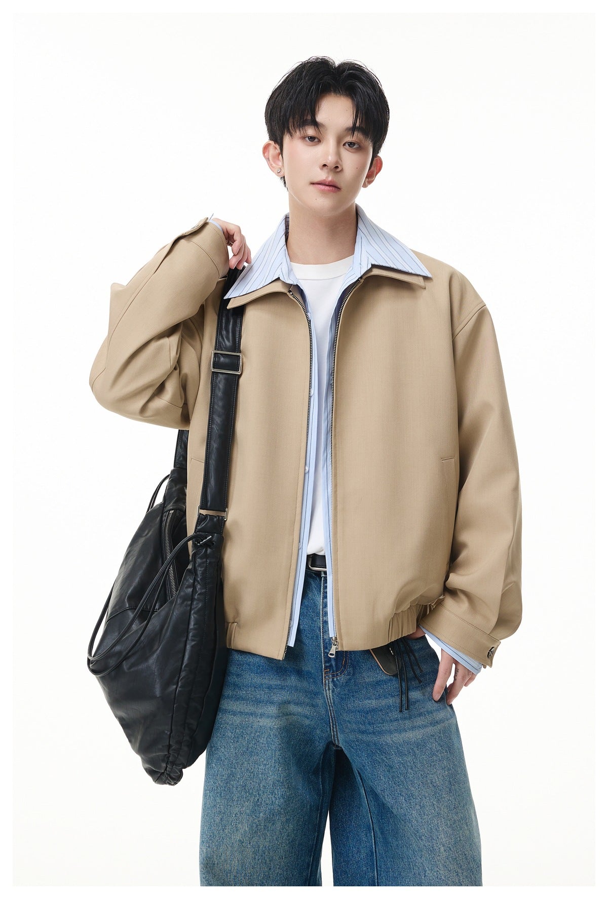 Model wearing a khaki zip jacket with striped shirt layer, white tee and jeans, carrying a black shoulder bag