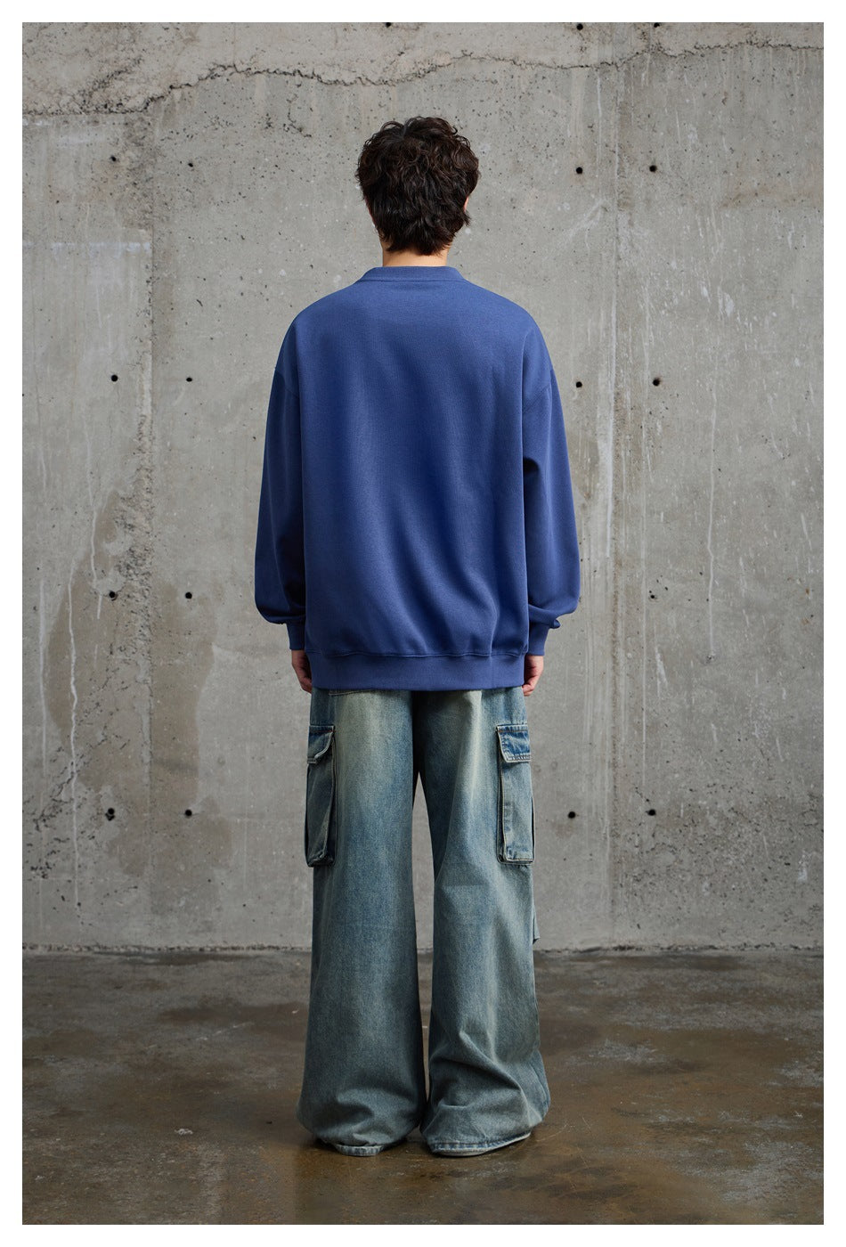 Rear view of a model wearing a plain blue oversized crewneck sweatshirt with ribbed cuffs and hem.
