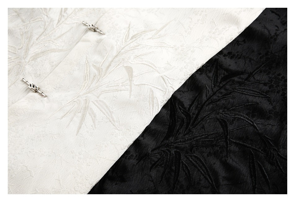 Close-up of ivory and black fabric with raised foliage embroidery and small silver frog-style fasteners.