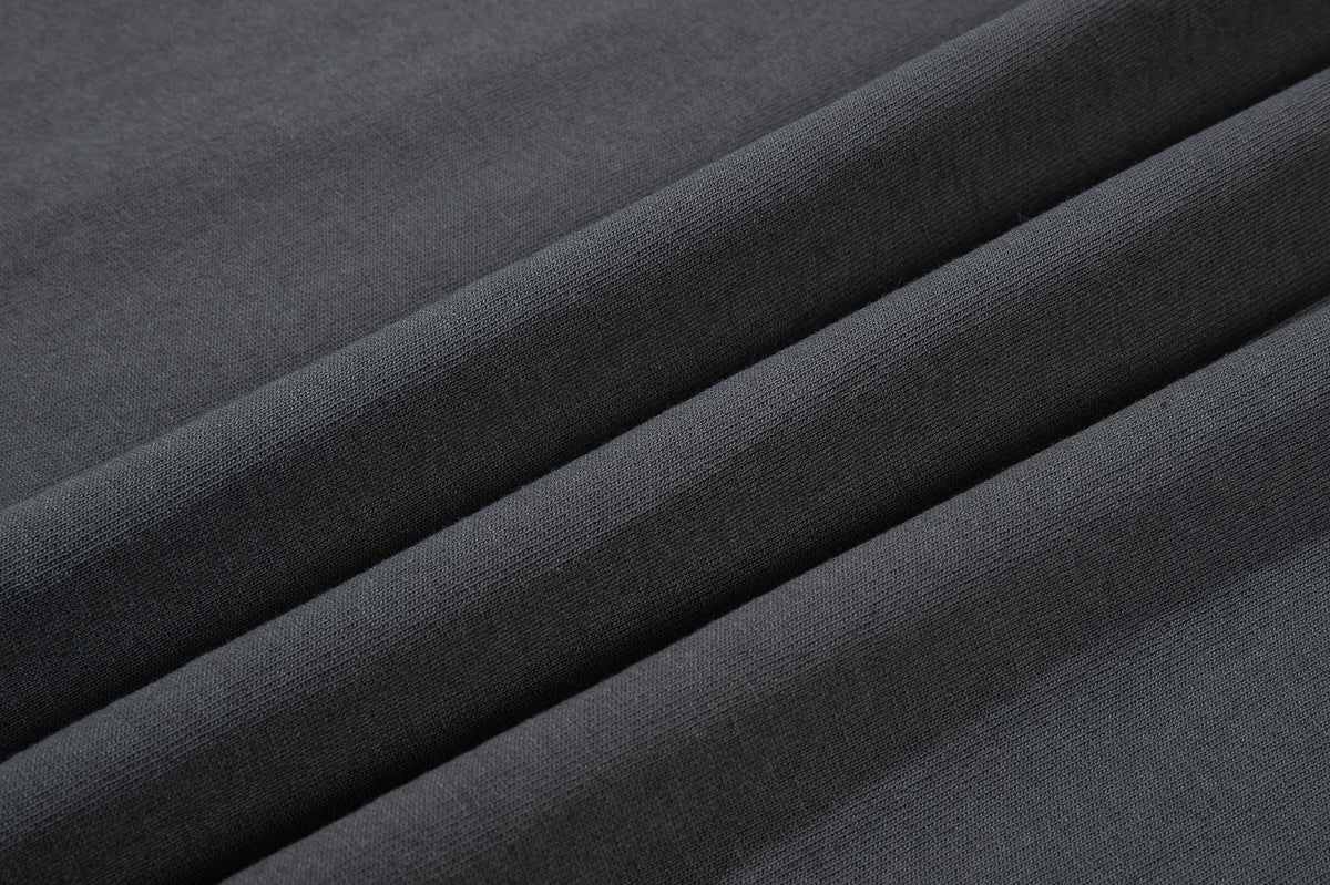 Close-up of charcoal gray knit fabric folded into diagonal ridges, showing its fine surface texture.
