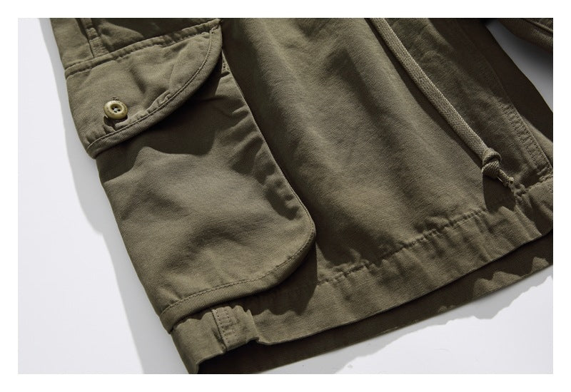 Close-up of olive cargo shorts showing a flap side pocket with button, drawstring, and hem stitching.