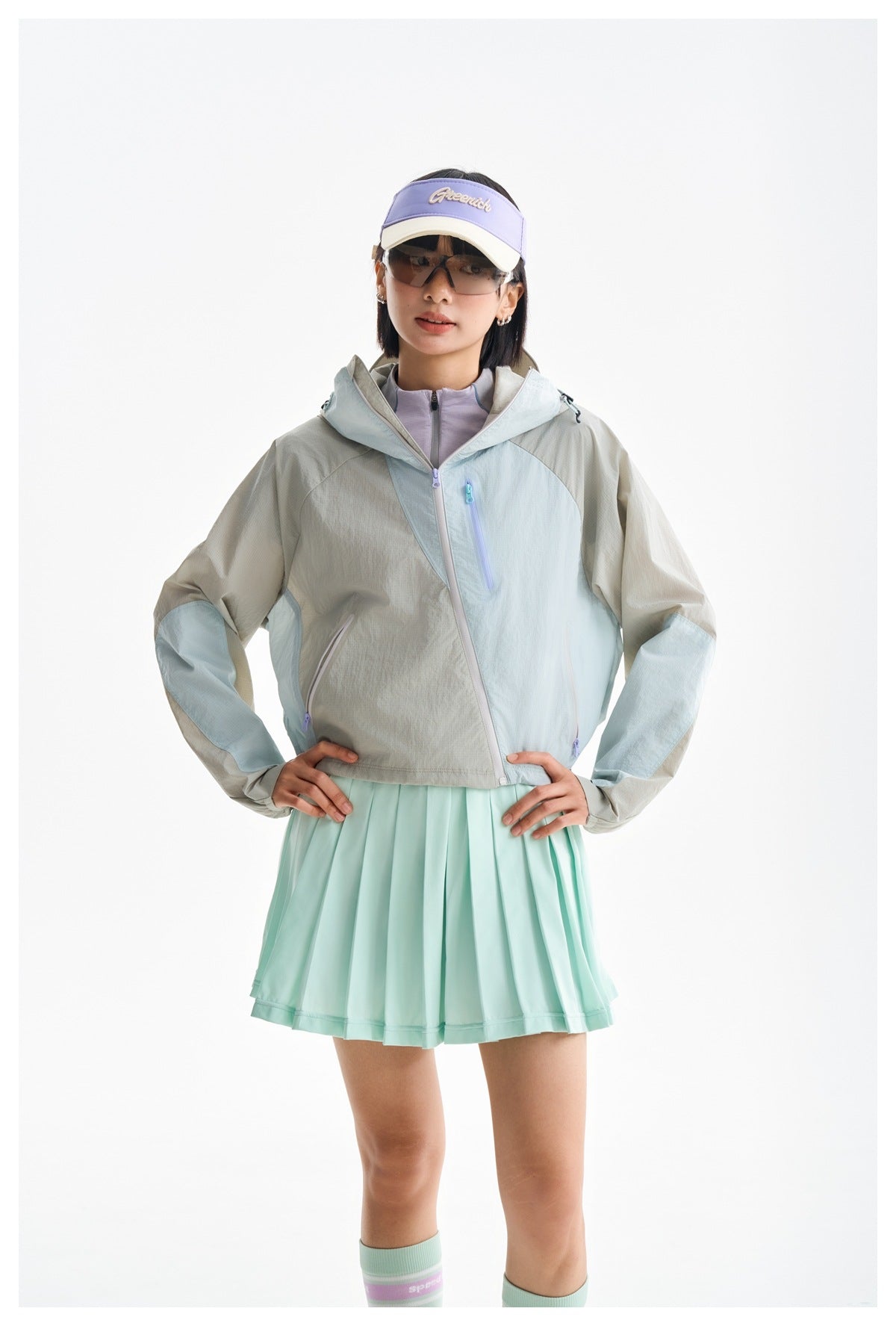Front view of a model wearing a gray and pale blue hooded jacket over a mint pleated skirt.