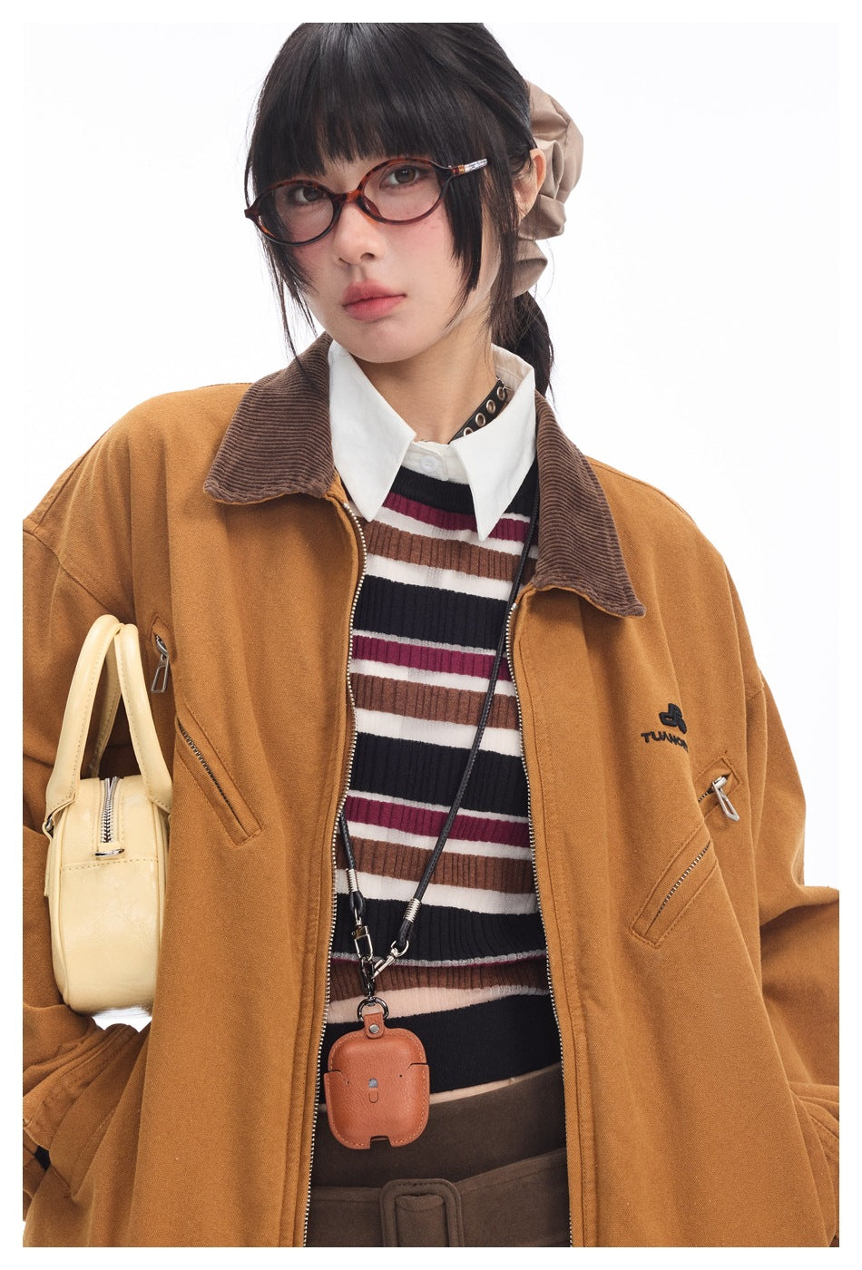 Close-up of a model wearing a mustard jacket with a brown collar over a multicolored striped top.