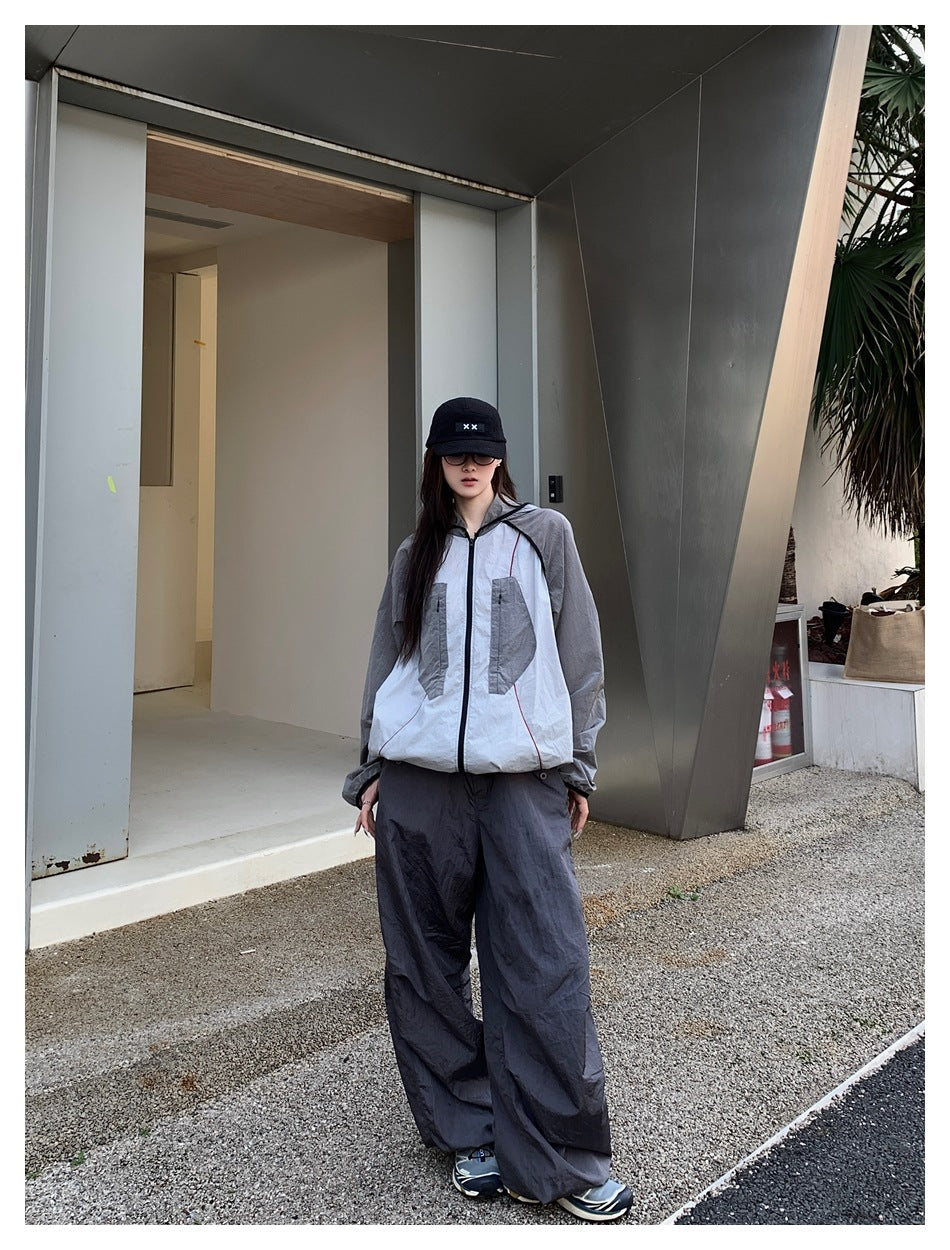 Model wearing the gray and white hooded zip jacket with wide gray trousers and a black cap outside a modern building
