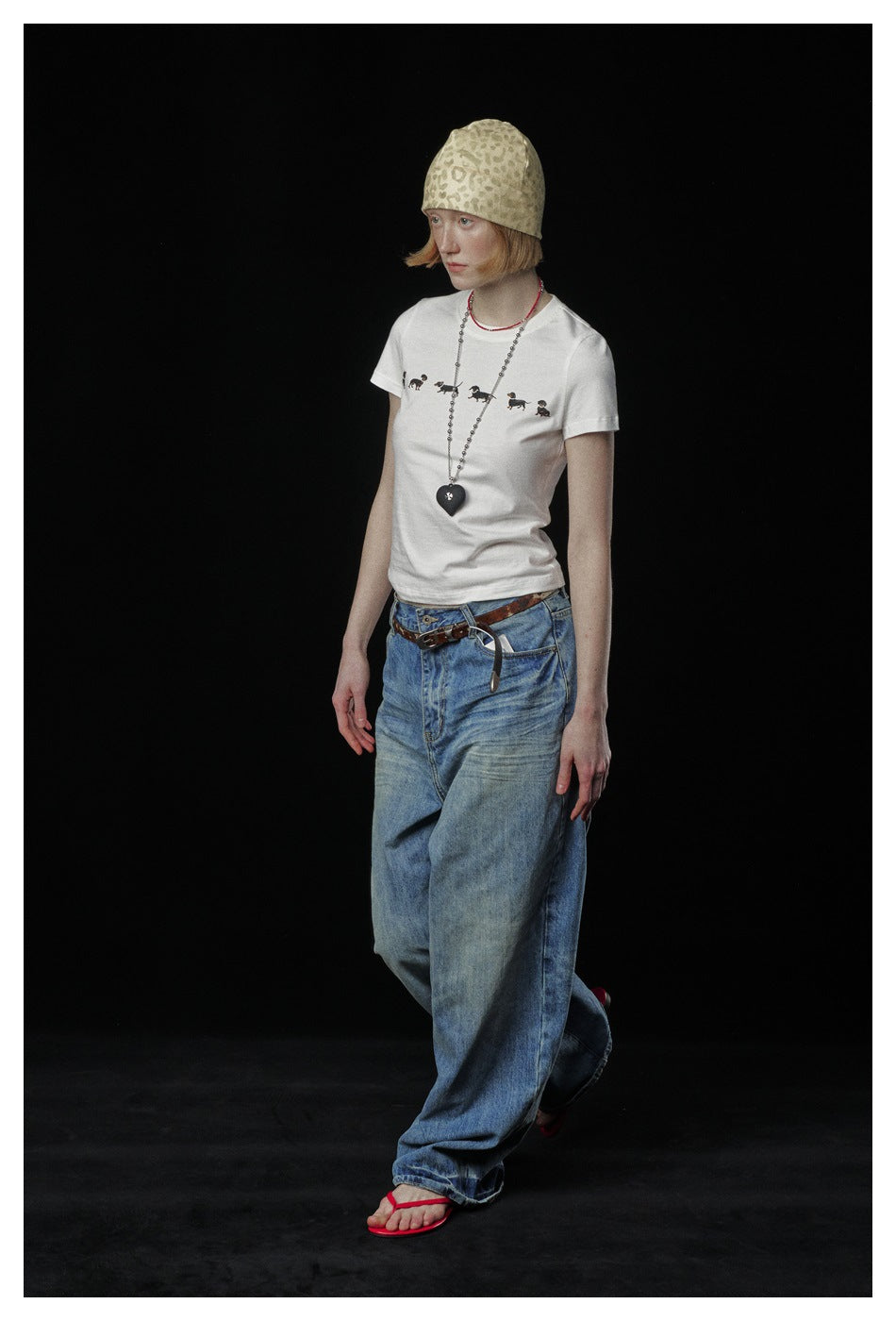 Full-length model in a white dog-print T-shirt, loose blue jeans, beige patterned beanie and red flip-flops.
