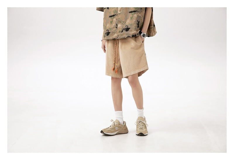 Cropped model wearing light tan knee-length shorts with a colorful braided drawstring, shown from the front.