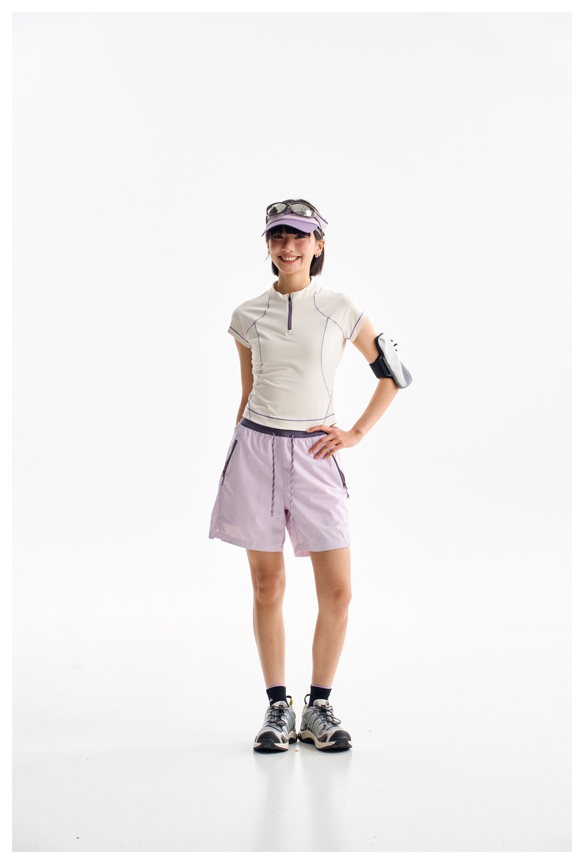 Model wearing a white zip-neck top with lavender piping and lavender shorts, visor, and running shoes.