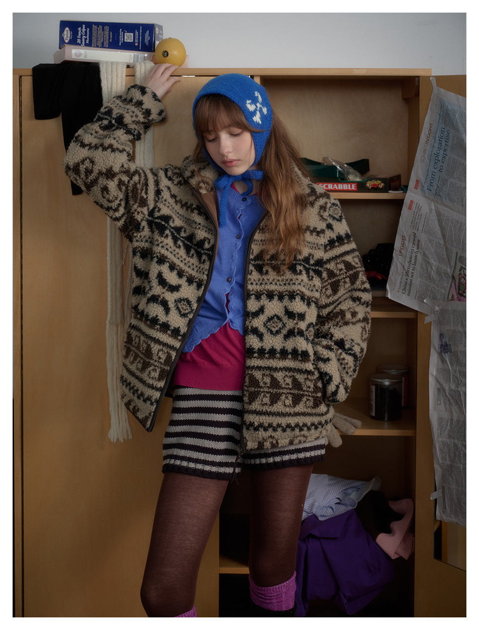 Model wearing an open beige-and-black patterned zip jacket over a blue top and striped shorts.