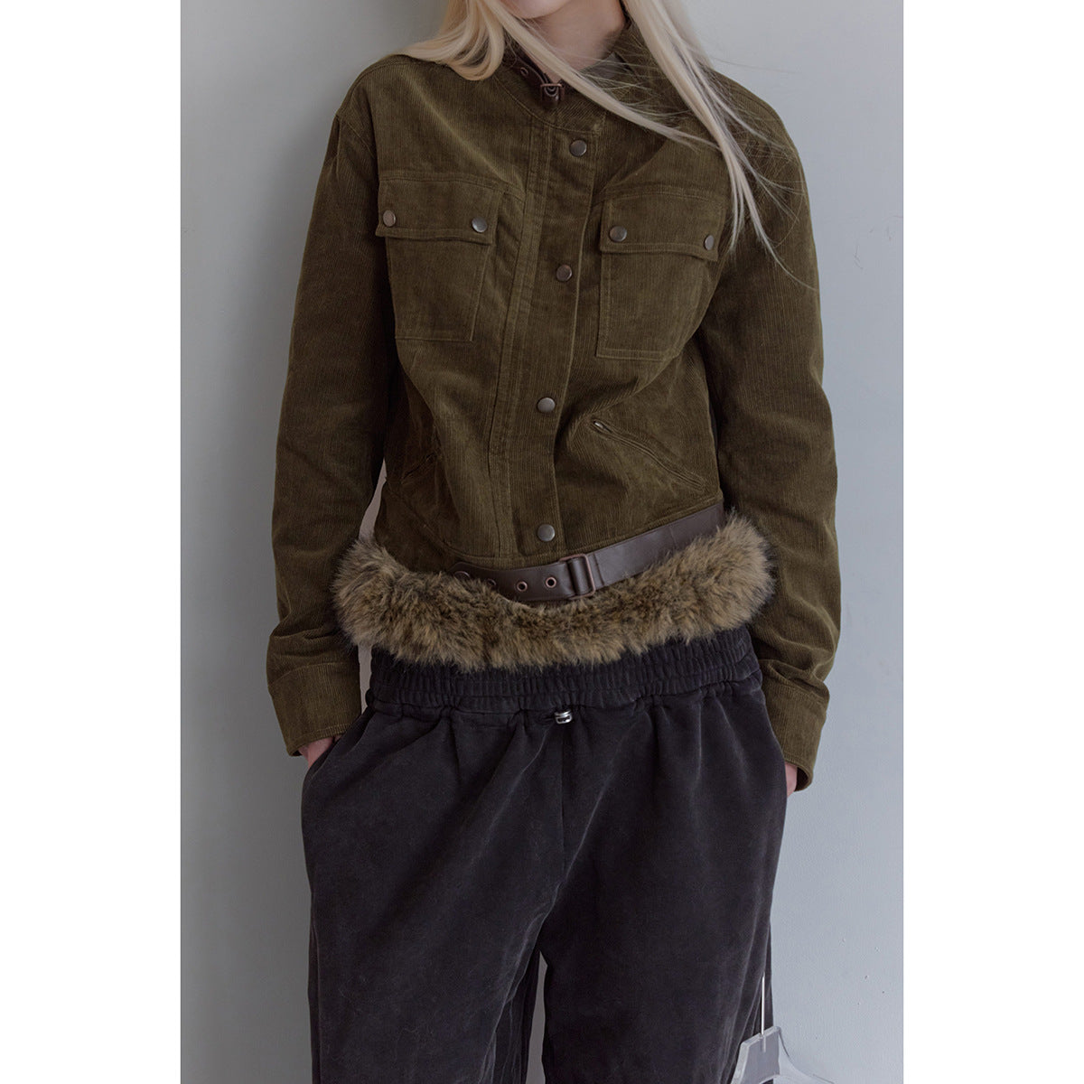Cropped view of a model wearing an olive jacket with snap-button chest pockets, a brown belt and fur-trimmed hem.
