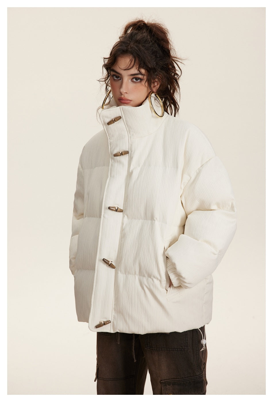 Model wearing a closed ivory quilted puffer jacket with a high stand collar and brown toggle fasteners.