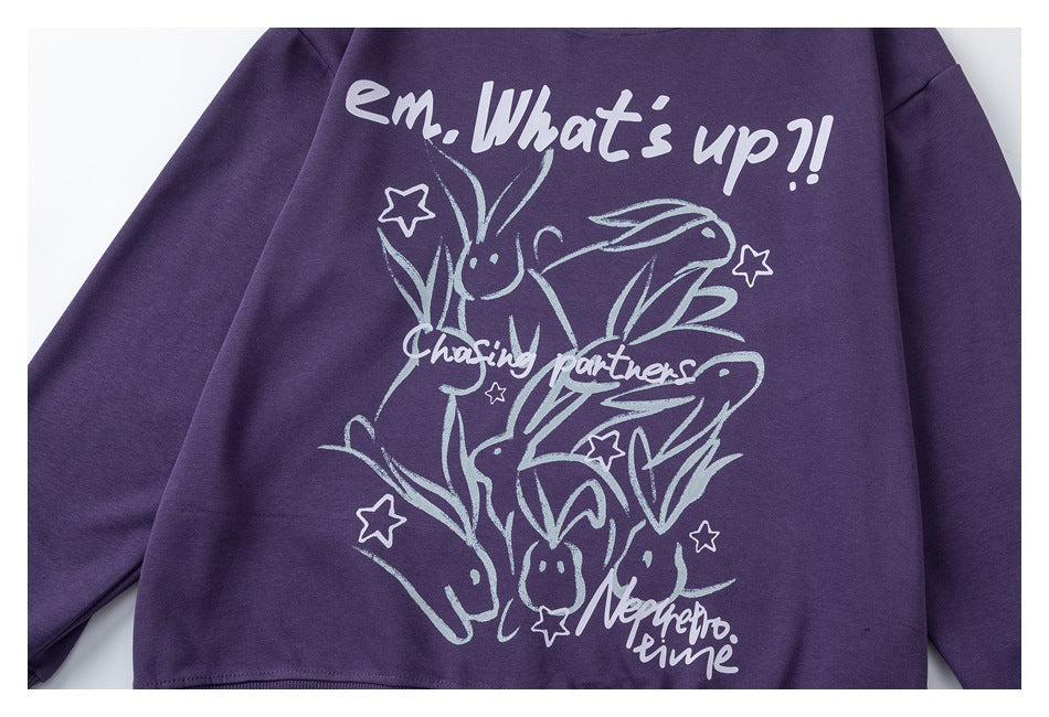 Close-up of a purple sweatshirt's front, showing a large pale graphic with lettering, stars, and playful figures.