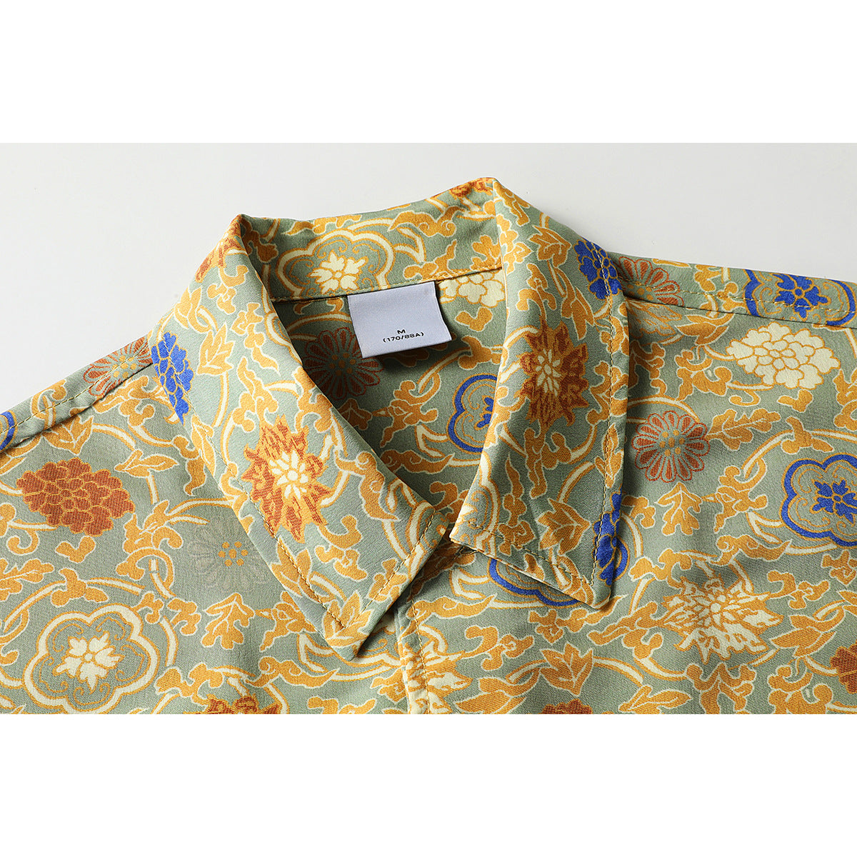 Close-up of a sage-green short-sleeve shirt collar with an ornate multicolor floral print and a size label.