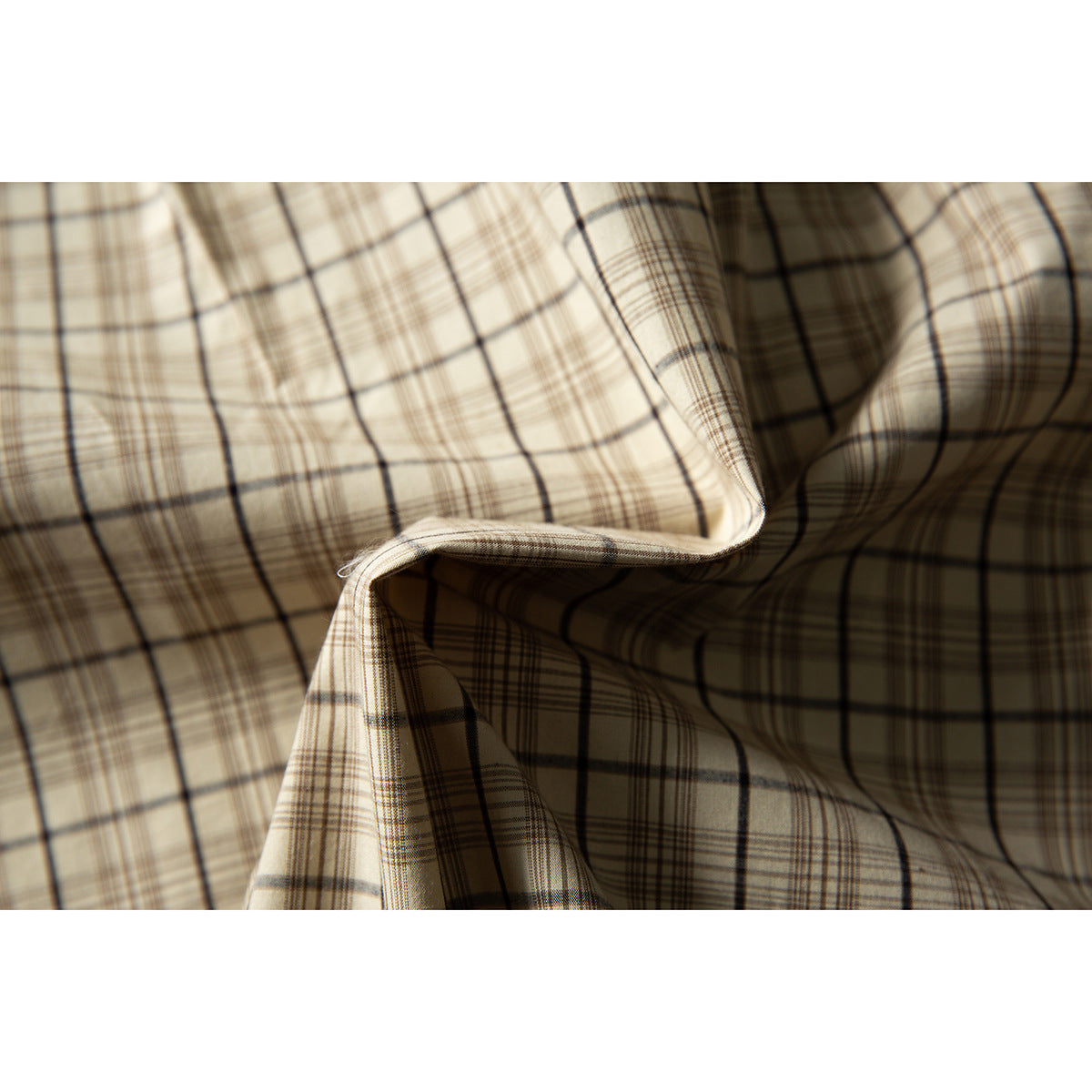Close-up of draped beige plaid shirt fabric, showing the pattern and curved stitched edge.