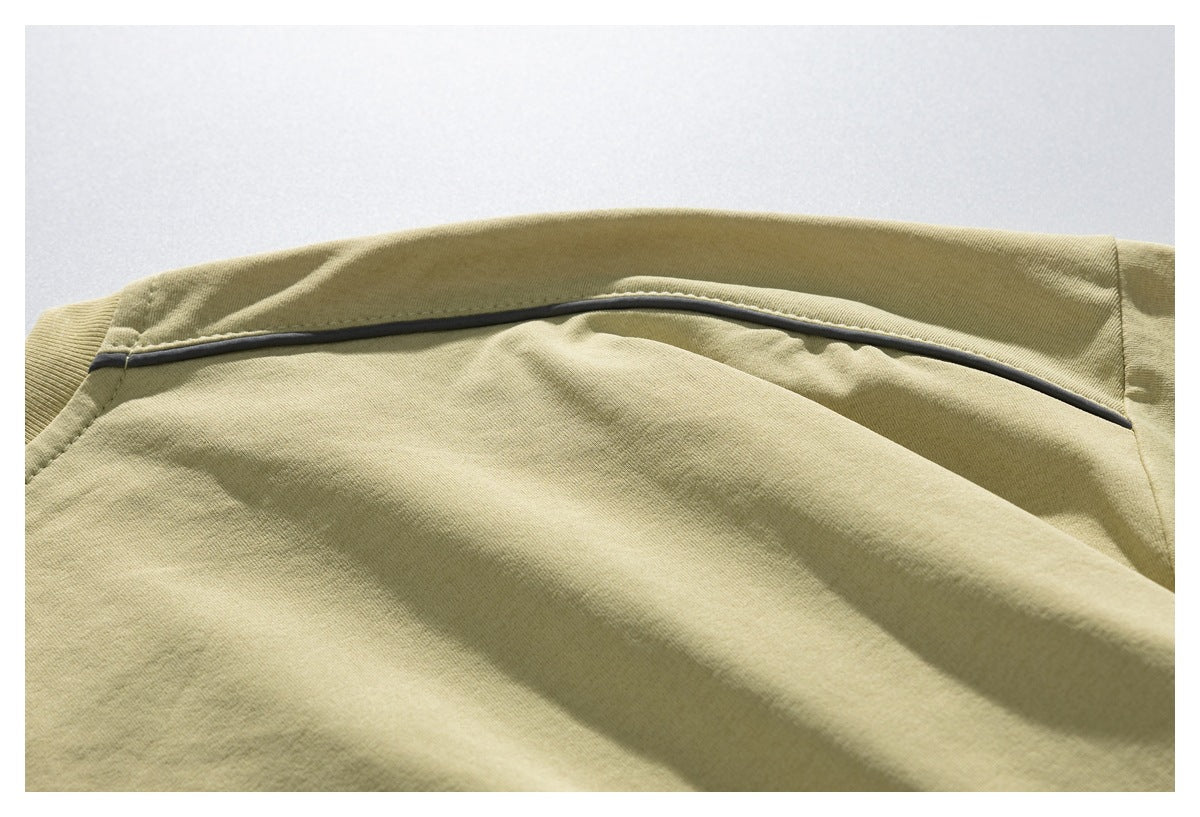 Close-up of a curved dark piping detail across the back shoulder of a pale olive T-shirt.