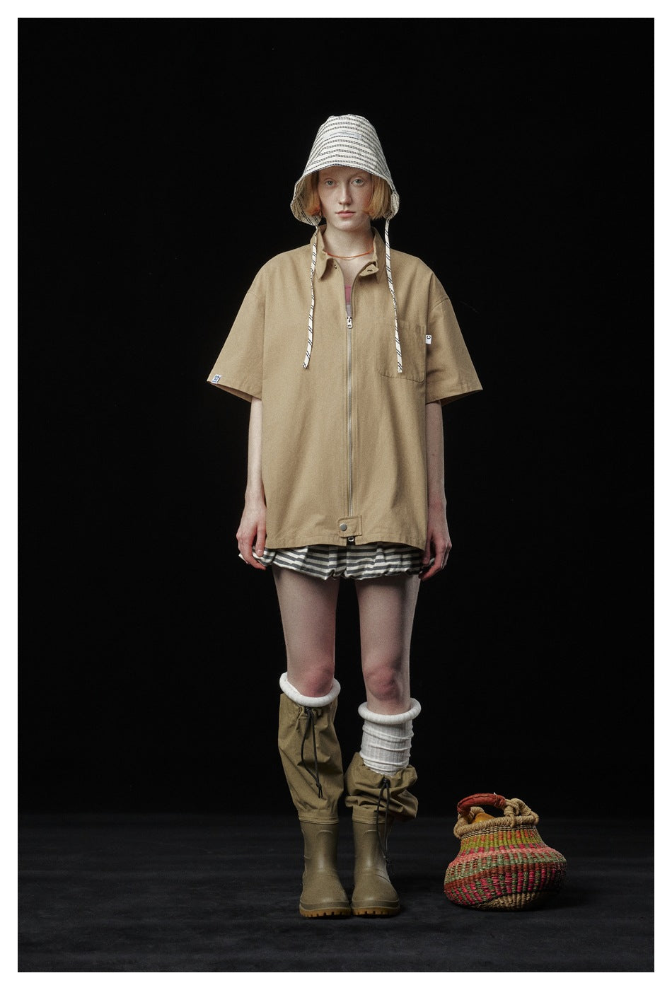 Full-length model wearing an oversized tan zip-front jacket with a striped bucket hat and shorts.