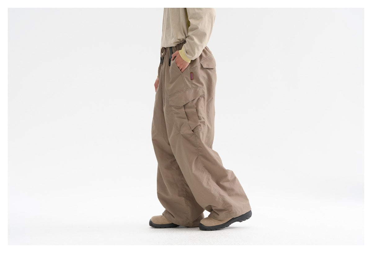 Side view of a model wearing loose taupe cargo pants with layered cargo pockets and a drawstring waist.