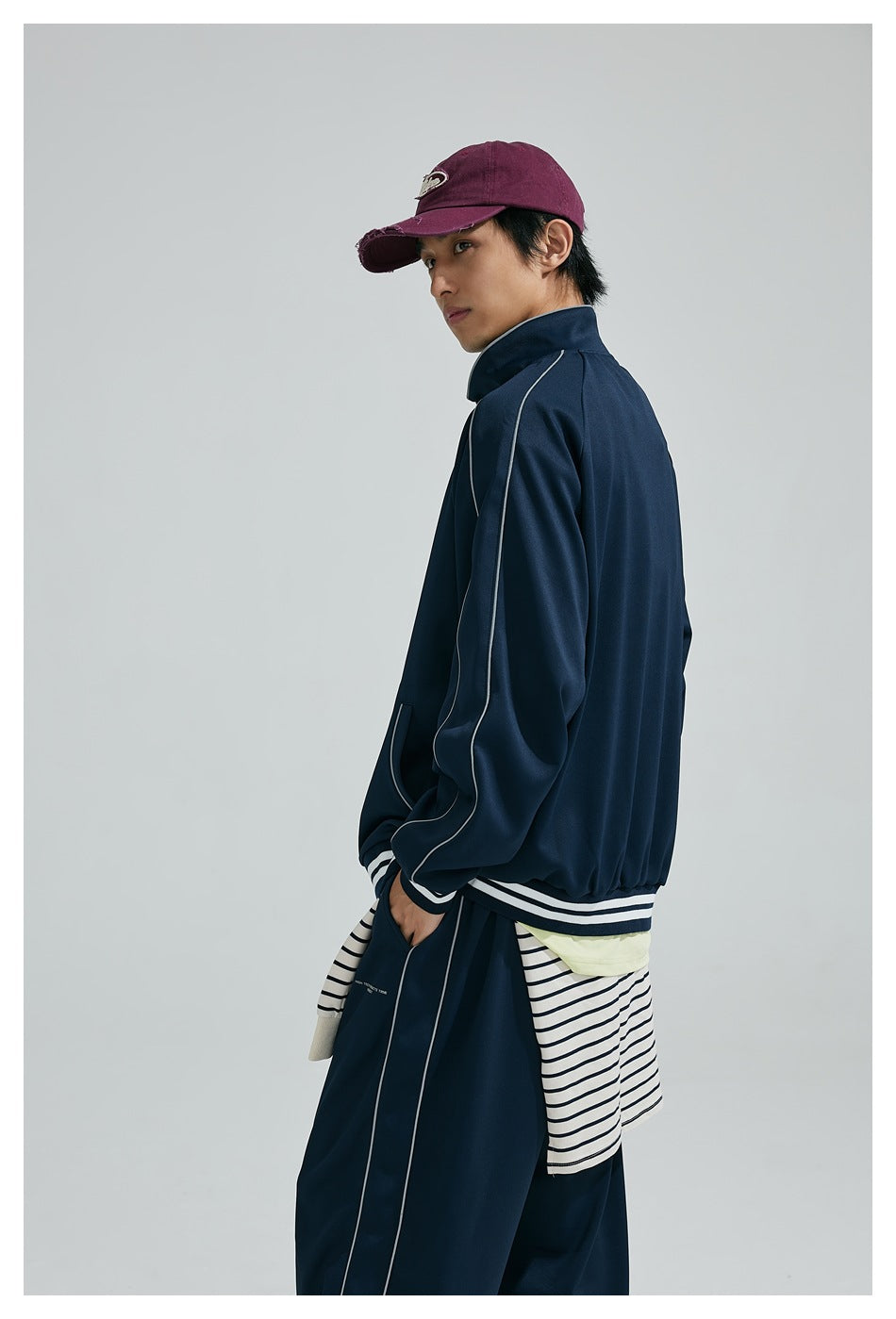 Model turned away to show the back of a navy track jacket with white piping and striped cuffs and hem.