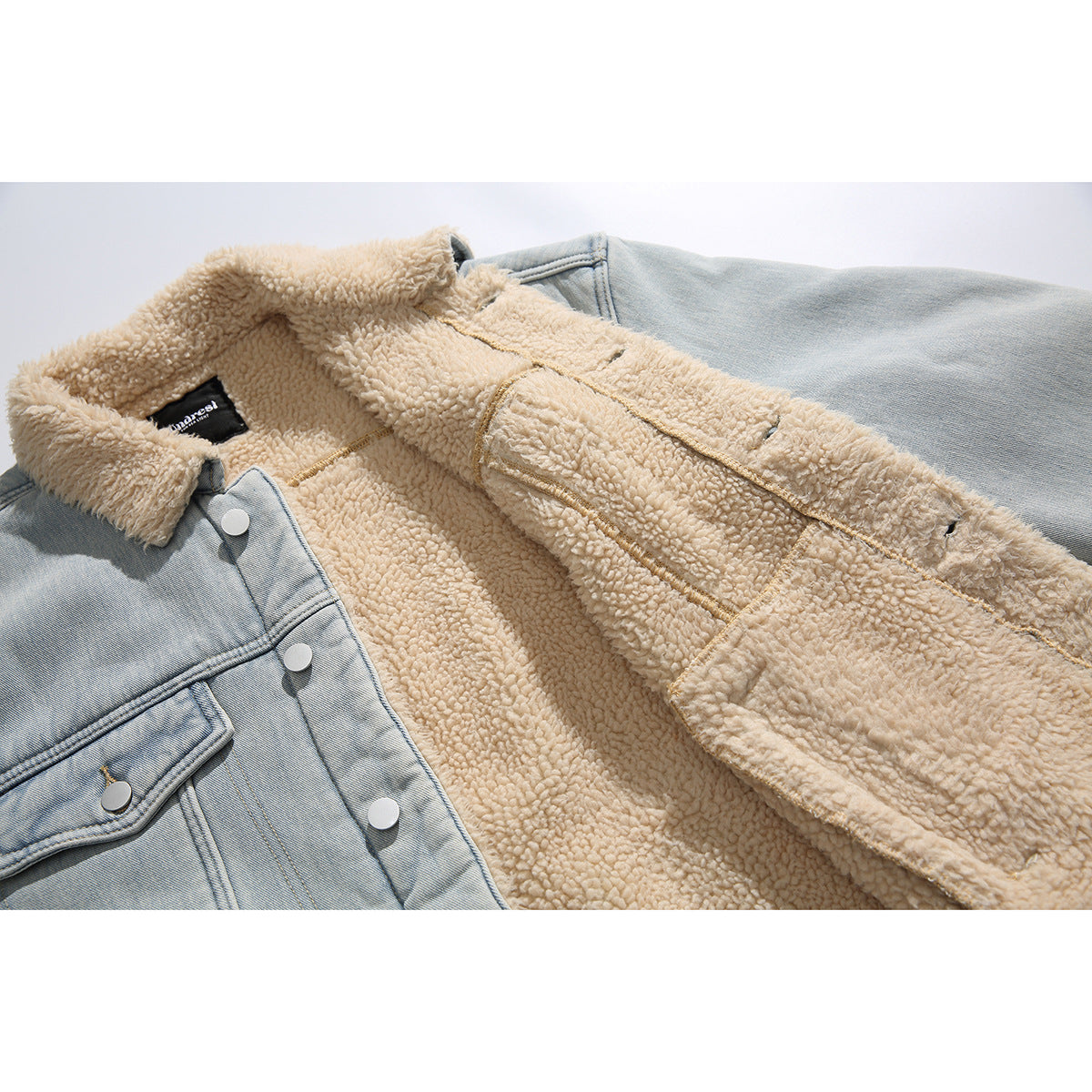 Close-up of a light blue denim jacket opened to show its cream sherpa lining, seams, buttons, and label.