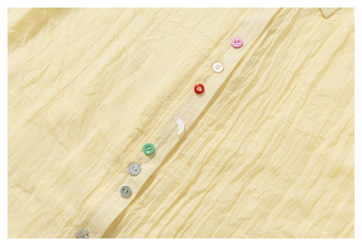 Close-up of a pale yellow shirt placket with assorted colorful buttons and softly crinkled fabric.