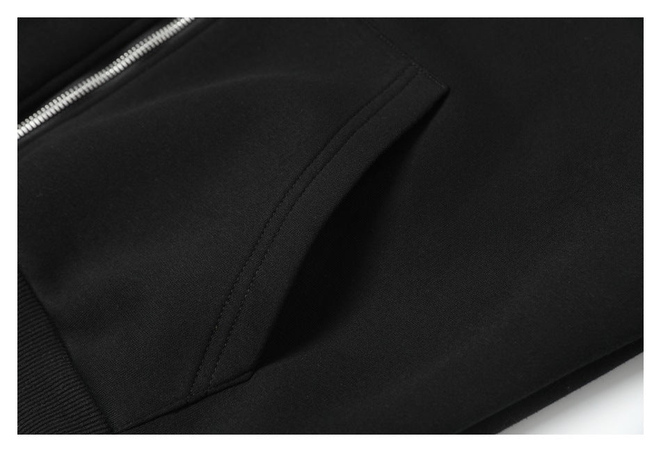Close-up of black hoodie fabric showing a curved seam, pocket edge, and silver zipper.
