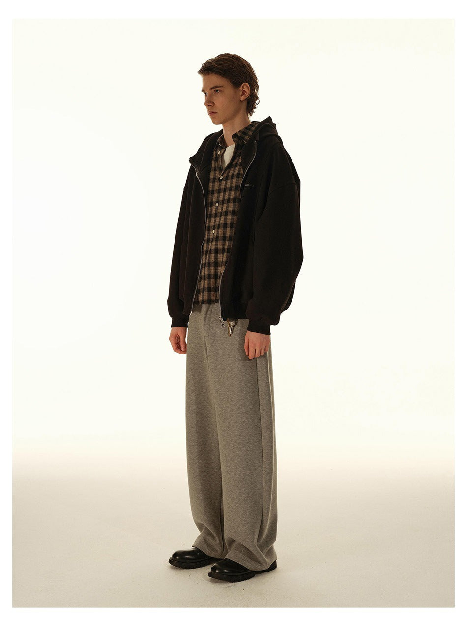 Model wearing an open black zip-up hoodie over a brown plaid shirt and wide-leg gray pants.