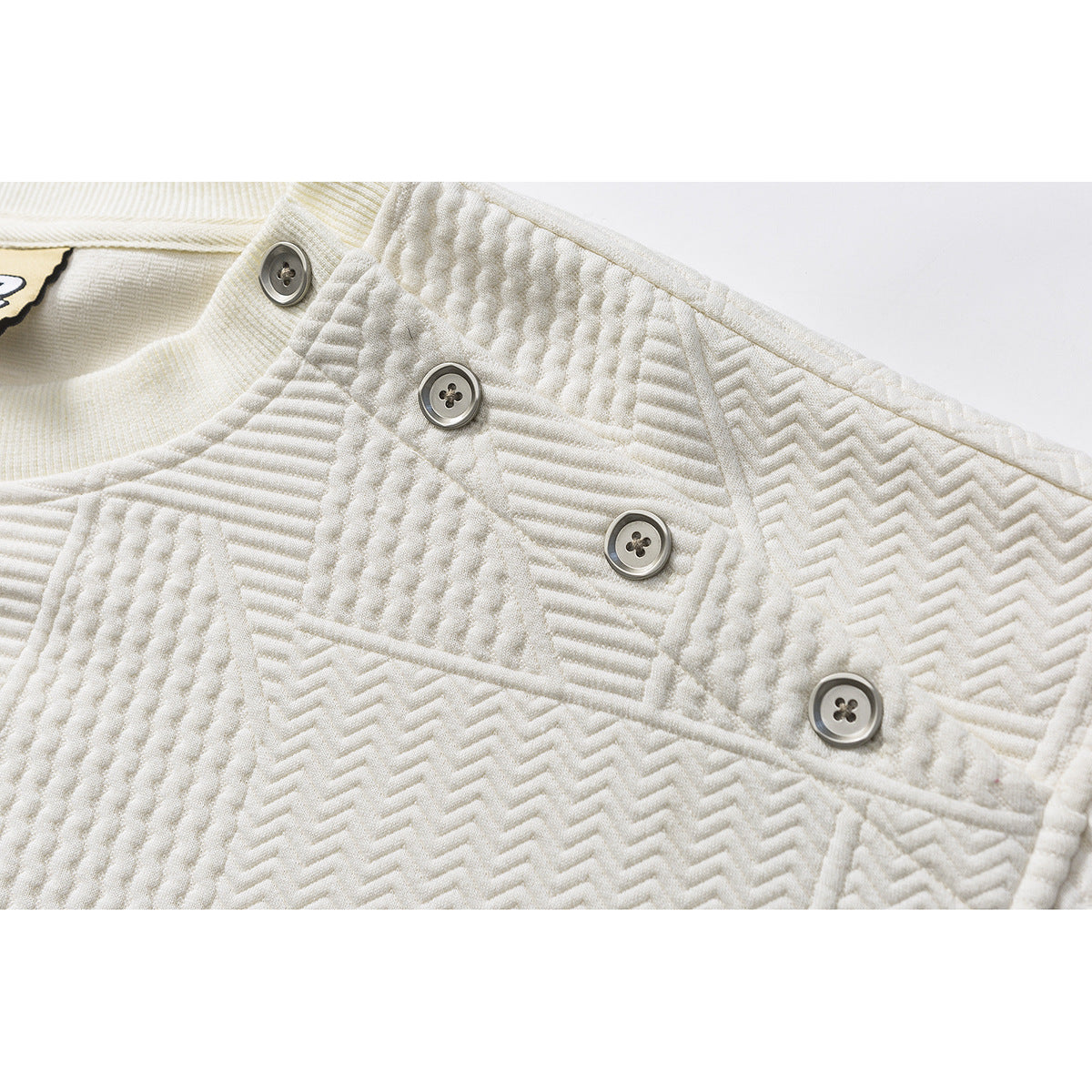 Close-up of an ivory pullover's shoulder placket with four gray buttons and raised geometric stitching.