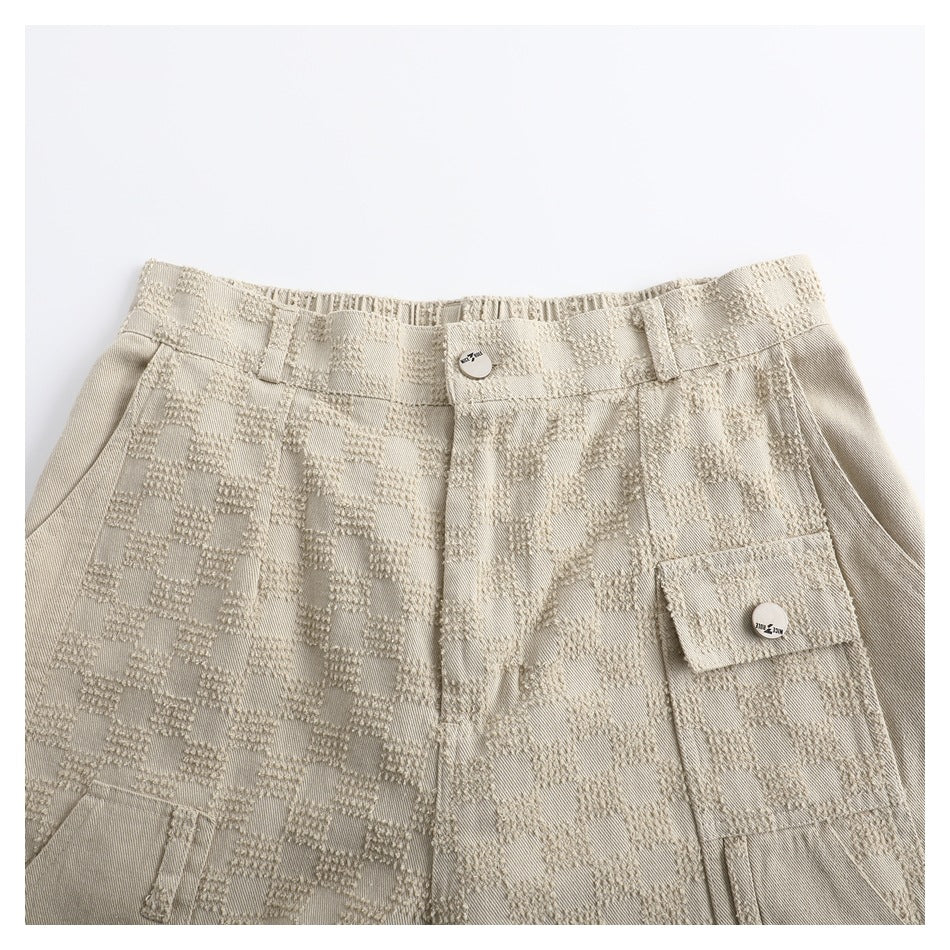 Close-up of beige check-textured cargo trousers showing the front waistband, fly, belt loops and flap pocket.