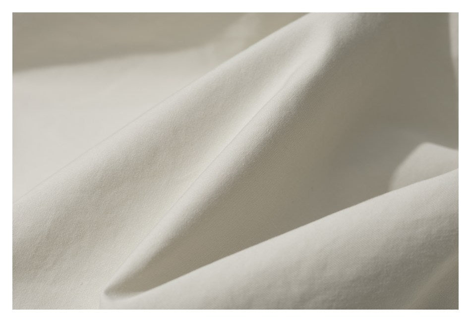 Close-up of ivory fabric folded into soft ridges, showing a fine, subtle woven texture.