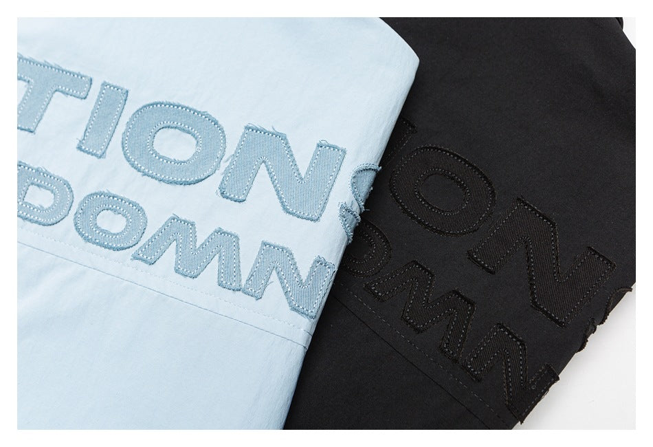 Close-up of light blue and black shirt sections with large matching-color stitched lettering.